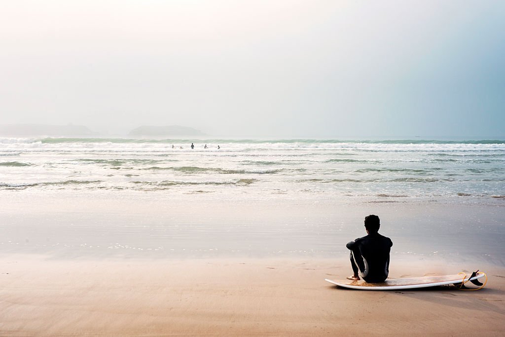 Man sitting on beach by surfboard